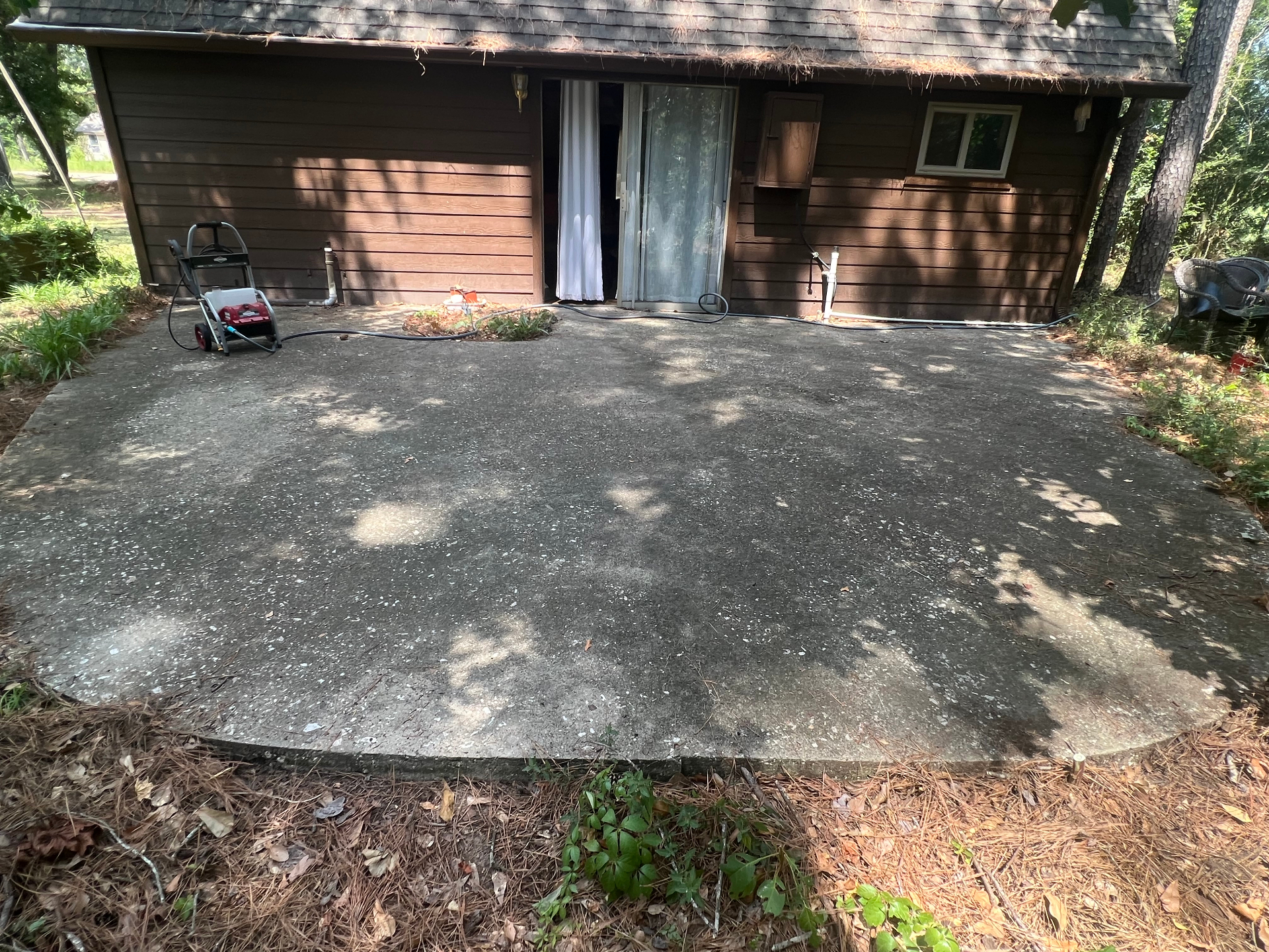 Dirty untreated concrete patio before cleaning, July 2023, with pressure washer in frame